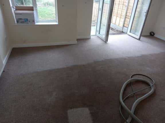 This is a photo of a living room that has been cleaned by K&S Carpet Cleaning, it is a brown carpet, and you can see a before and after shot, where one part has been cleaned.